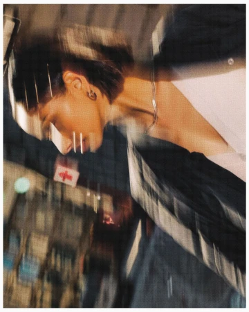 Blurred view of a fashion model in an urban setting, styled with a hair clip and jewelry; motion creates dynamic energy.