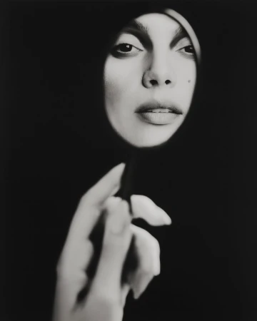 Close-up portrait of Charlee Fraser looking into a small circular mirror held by her hand against a dark background
