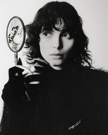 A portrait of a brunette woman holding a vintage mirror with a butterfly design, against a plain white backdrop, close-up.