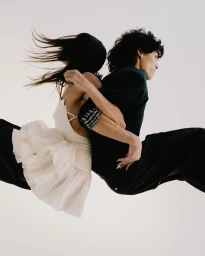Two models suspended mid-air back-to-back in dynamic motion against a bright off-white studio background.