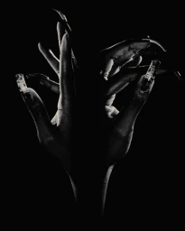 Dramatic black and white photograph of hands with long sculpted nails posed together against a solid black background.
