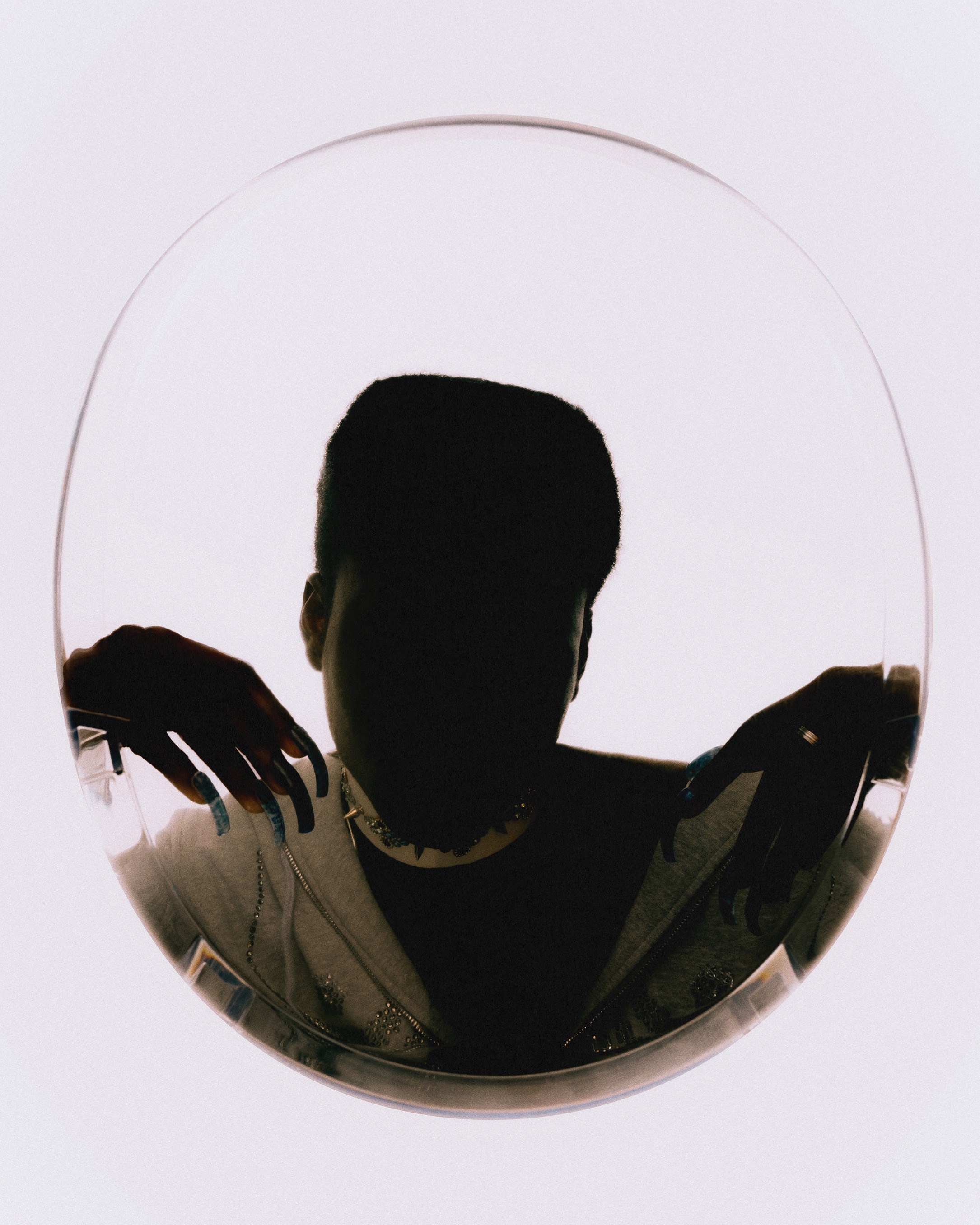Person framed in a circular transparent panel, wearing a patterned jacket and statement necklace, with a light background.