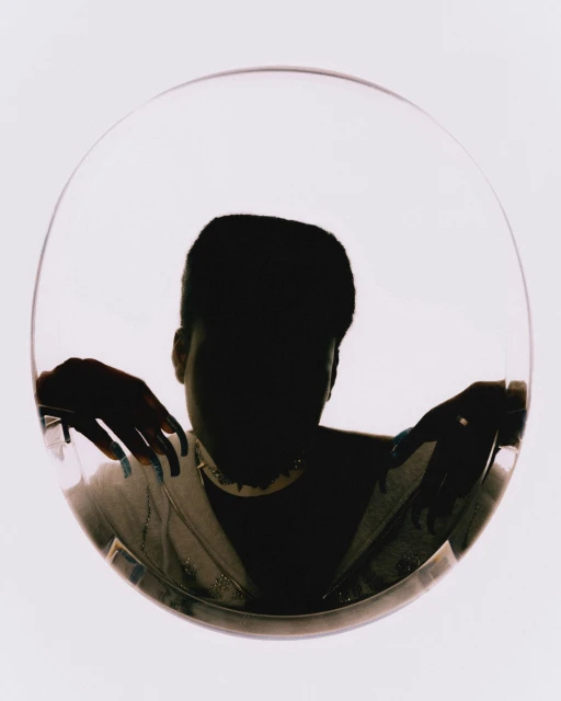 Person framed in a circular transparent panel, wearing a patterned jacket and statement necklace, with a light background.