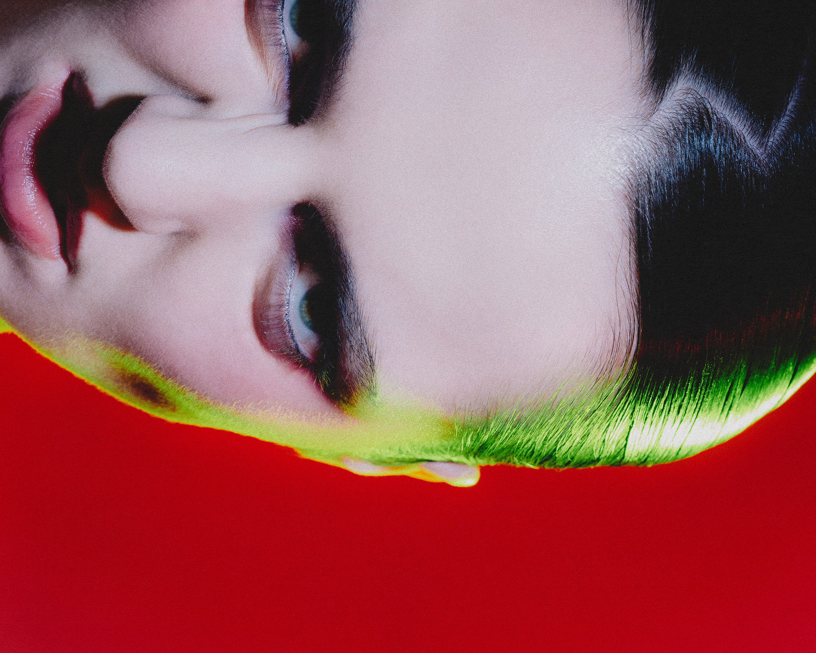 Close-up portrait of a woman lying down with vibrant green hair and red backdrop, focusing on her face and striking beauty.