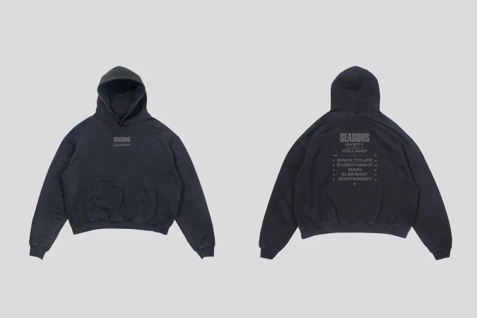Two dark-gray hooded sweatshirts, one facing forward and one facing back, displayed on a light-gray studio backdrop with soft, neutral lighting.