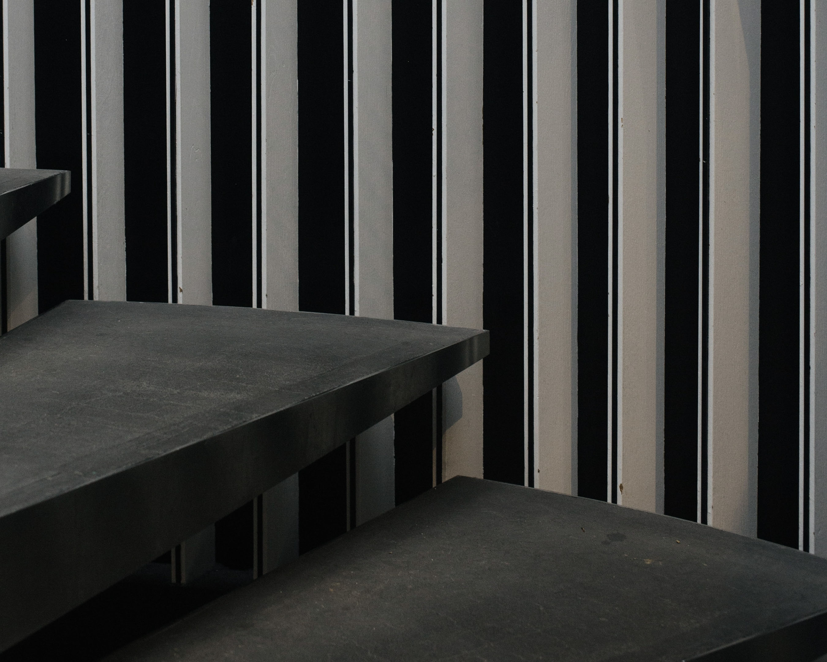 Abstract view of an interior featuring black and white striped wall, and gray stairs in the foreground, creating an interesting geometric pattern.