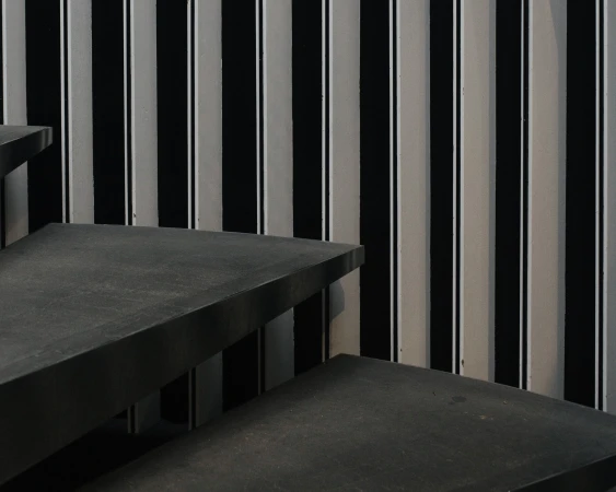 Abstract view of an interior featuring black and white striped wall, and gray stairs in the foreground, creating an interesting geometric pattern.