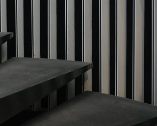 Dark floating stone staircase steps set against a high-contrast black and white vertically striped architectural wall.