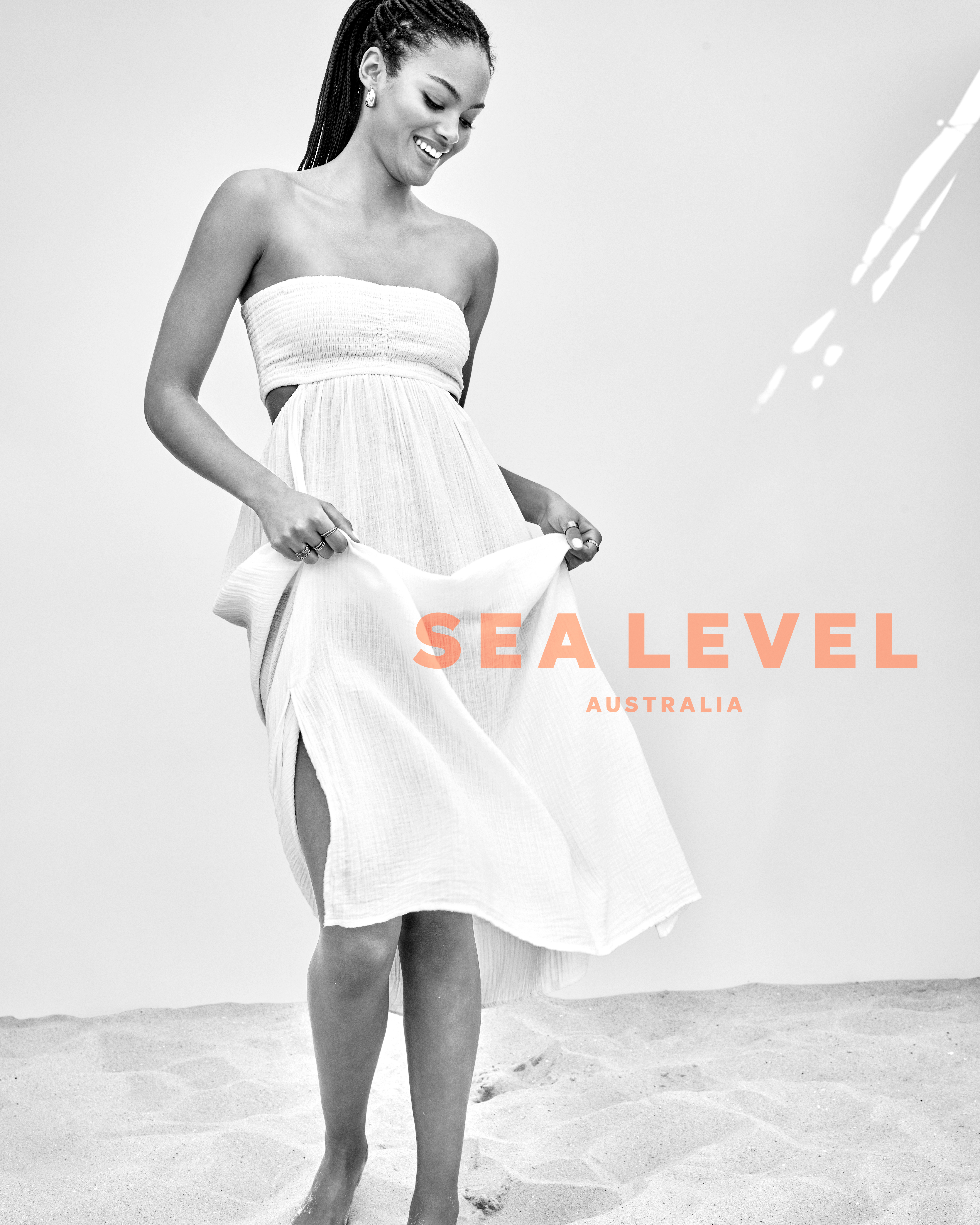 A smiling woman poses on a beach in a white, strapless dress. The background is a light grey, with 'SEA LEVEL AUSTRALIA' text overlay.