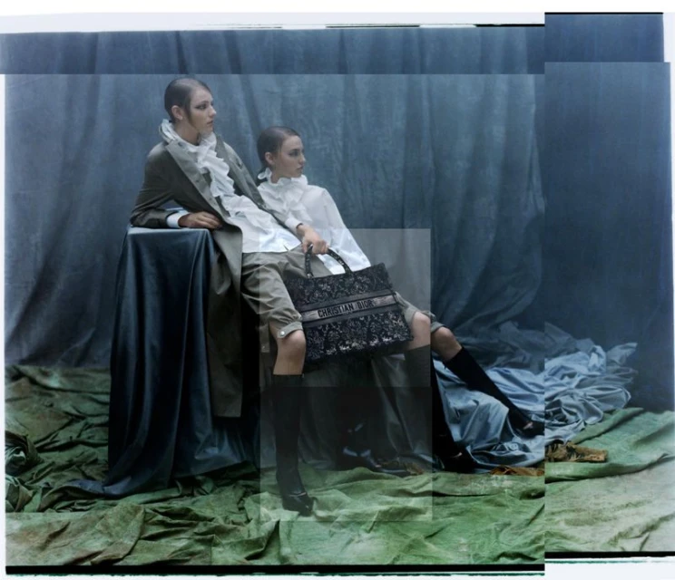 Two models pose in a photo studio with a Dior handbag. The scene features soft lighting, flowing garments, and draped fabric backgrounds.