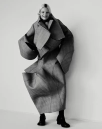 Model Mila van Eeten wearing an oversized structural grey coat against a white studio background for Purple Magazine.