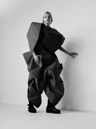 Mila van Eeten wearing an avant-garde geometric origami structured garment and platform boots in a monochrome studio setting.