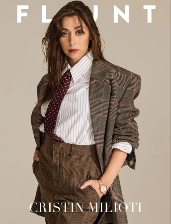 Cristin Milioti gazes with a serious expression, wearing a striped shirt, tie, plaid suit and pants against a neutral backdrop, photographed indoors.