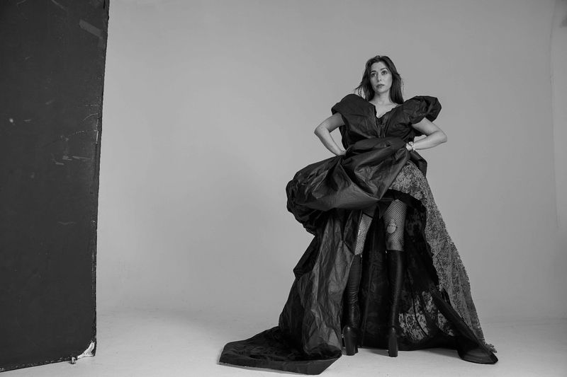 Woman in elaborate black gown poses in a photo studio with theatrical flair. Tulle and lace detail visible with dark dramatic lighting.