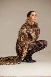 Cristin Milioti wearing a leopard print faux fur coat and black lace patterned tights crouching in a studio.