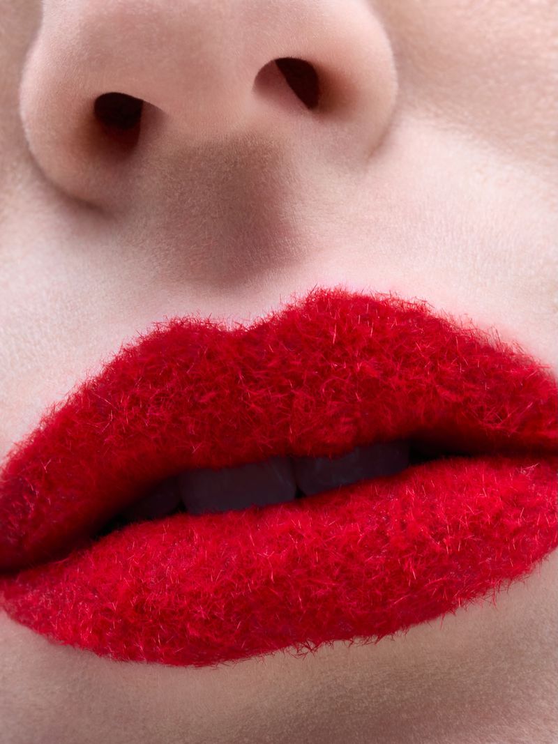 Close-up shot of a person's face, focusing on the nose and mouth with red, furry-textured lipstick emphasizing a unique, textured beauty concept.
