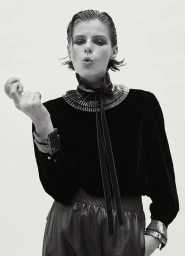 Model with slicked-back dark hair wearing a ruffled velvet blouse against a white background