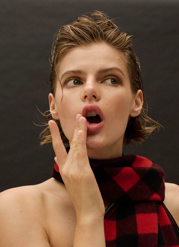 Portrait of a model with wet-look hair and a red and black plaid scarf against a dark background