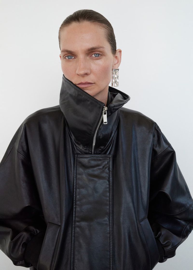 Portrait of a woman in a black leather jacket and silver earrings against a white background in a studio fashion shot.