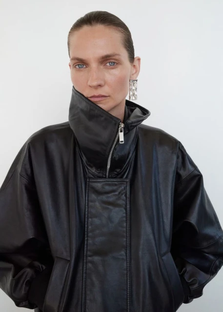 Portrait of a woman in a black leather jacket and silver earrings against a white background in a studio fashion shot.