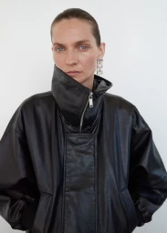Model Karolin Wolter wearing an oversized black leather jacket with a high funnel collar against a plain white studio background.