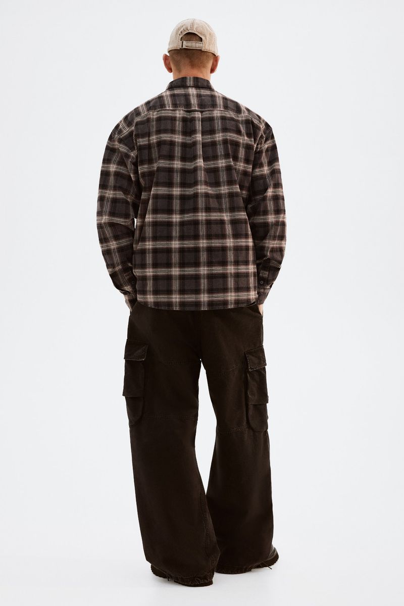 Back view of a slender adult male in a plaid flannel shirt, wide-leg cargo pants, and a baseball cap, standing on a white background.