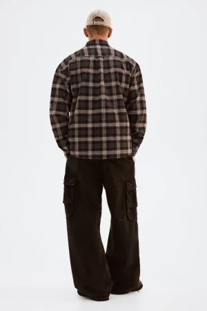 Back view of a slender adult male in a plaid flannel shirt, wide-leg cargo pants, and a baseball cap, standing on a white background.