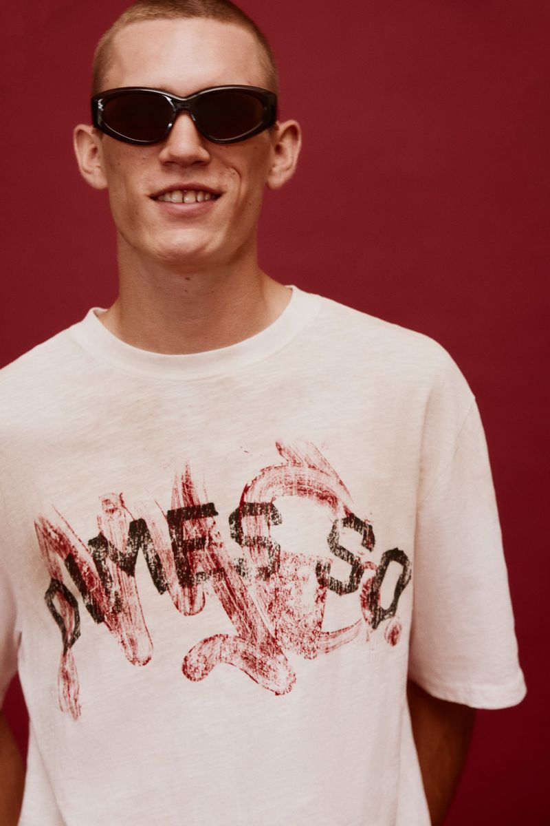 Stylish man in sunglasses and white graphic t-shirt against a red backdrop, posing for a studio portrait. Fashion and portrait photography.
