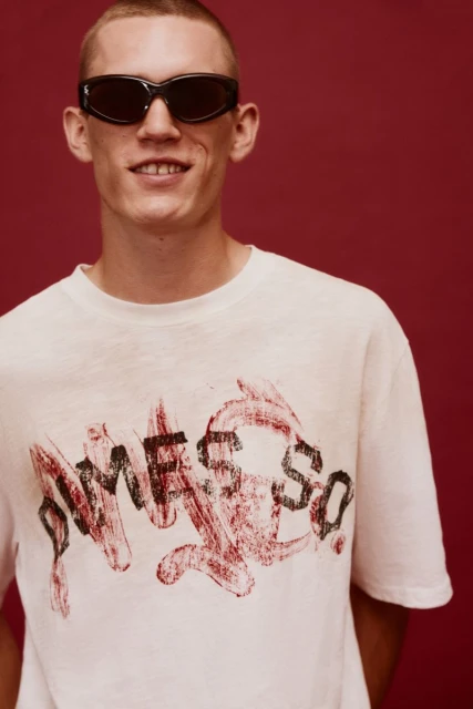 Stylish man in sunglasses and white graphic t-shirt against a red backdrop, posing for a studio portrait. Fashion and portrait photography.