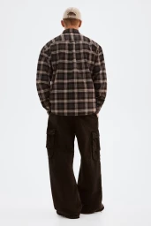 Model from the back wearing a plaid flannel shirt, dark cargo pants, and a baseball cap against a white background.