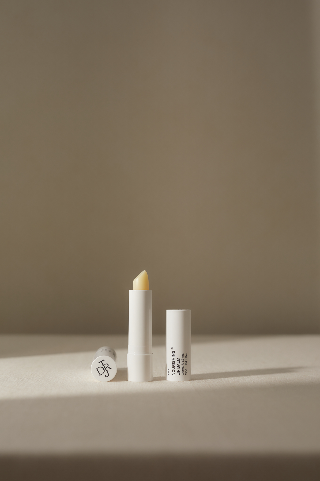 Product shot featuring three white tubes of nourishing lip balm, one open to display the balm, on a neutral surface.