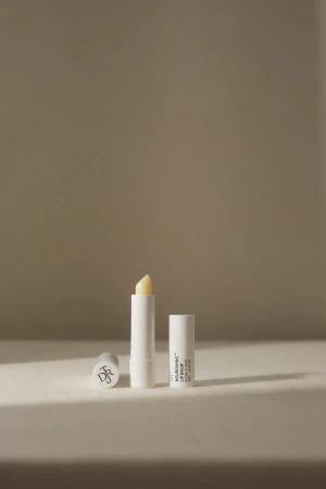 Product shot featuring three white tubes of nourishing lip balm, one open to display the balm, on a neutral surface.