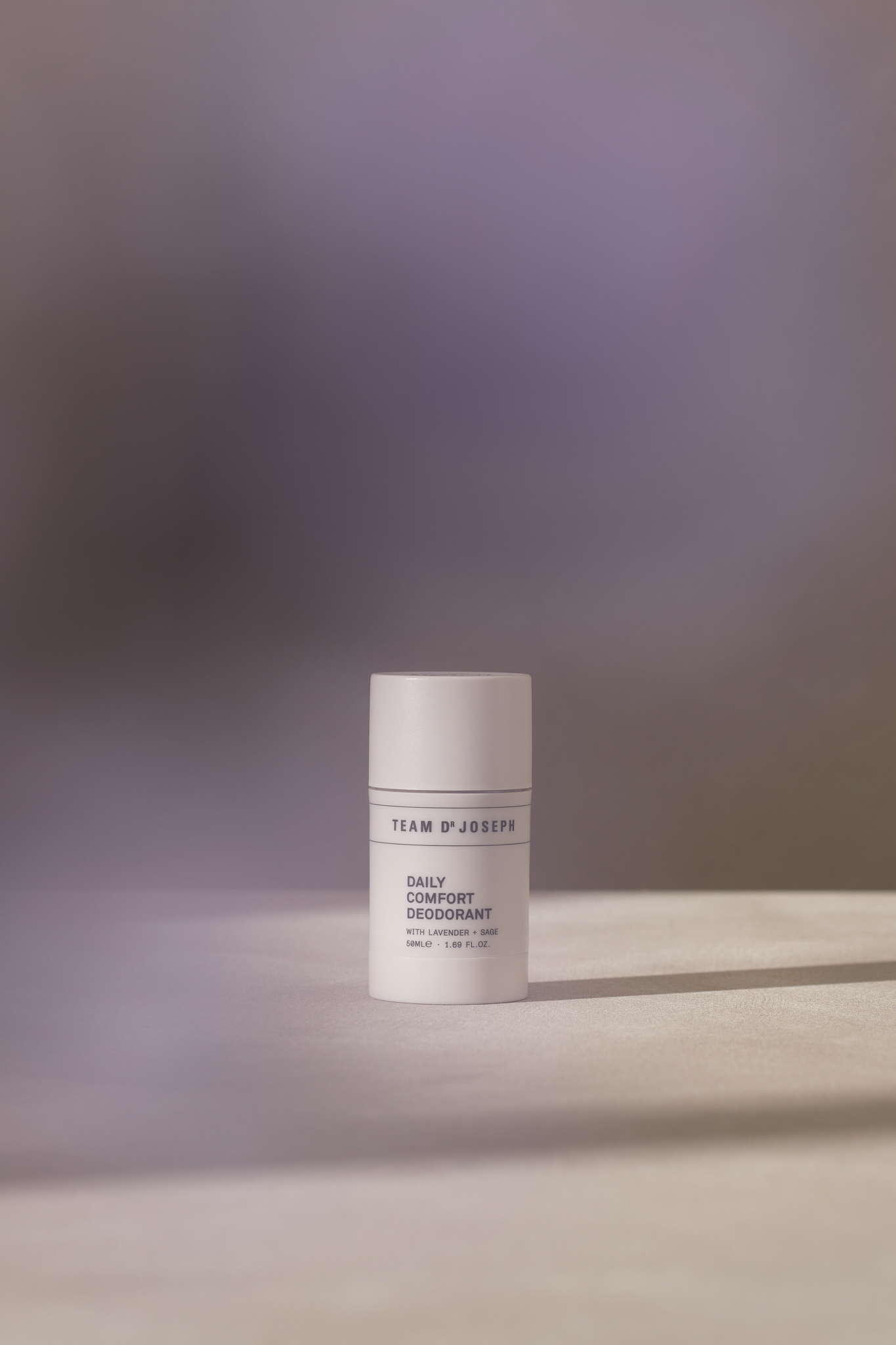 Studio shot of Team 8' Joseph's Daily Comfort Deodorant. White container with product information against a blurred, gradient background.