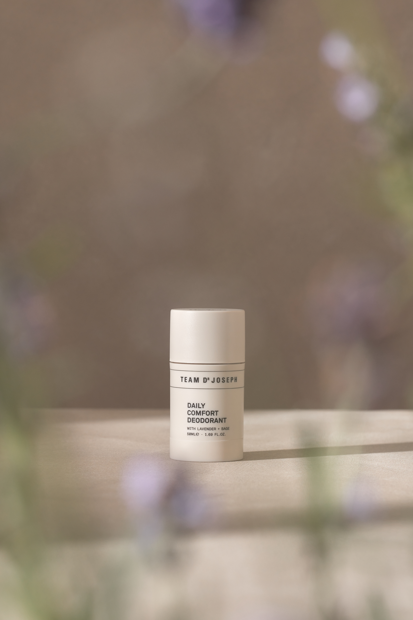 Beige deodorant stick stands on a light surface against a blurred background with floral accents, product shot, beauty concept.