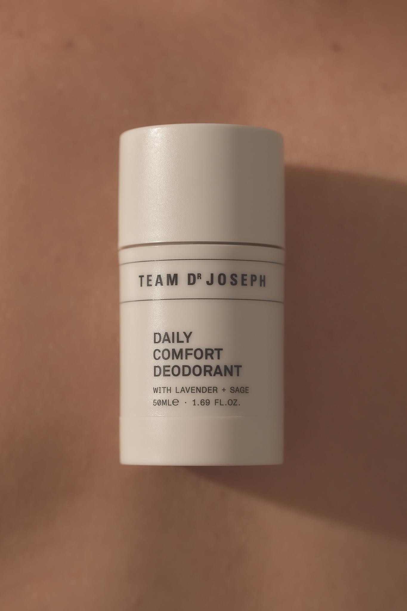 Close-up of a white container of Team D'Joseph Daily Comfort Deodorant against a light brown skin background, showcasing beauty product.