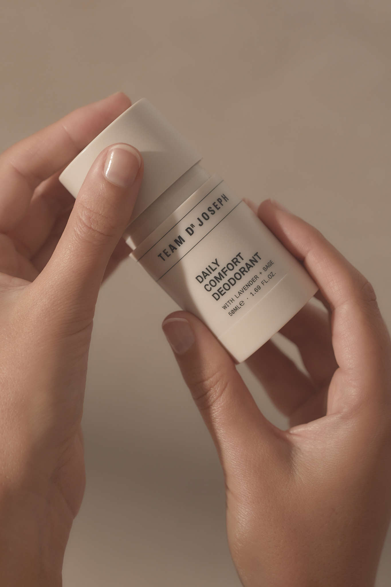 A deodorant stick is held in two hands indoors against a neutral background, showcasing a minimalist package design and skincare concept.