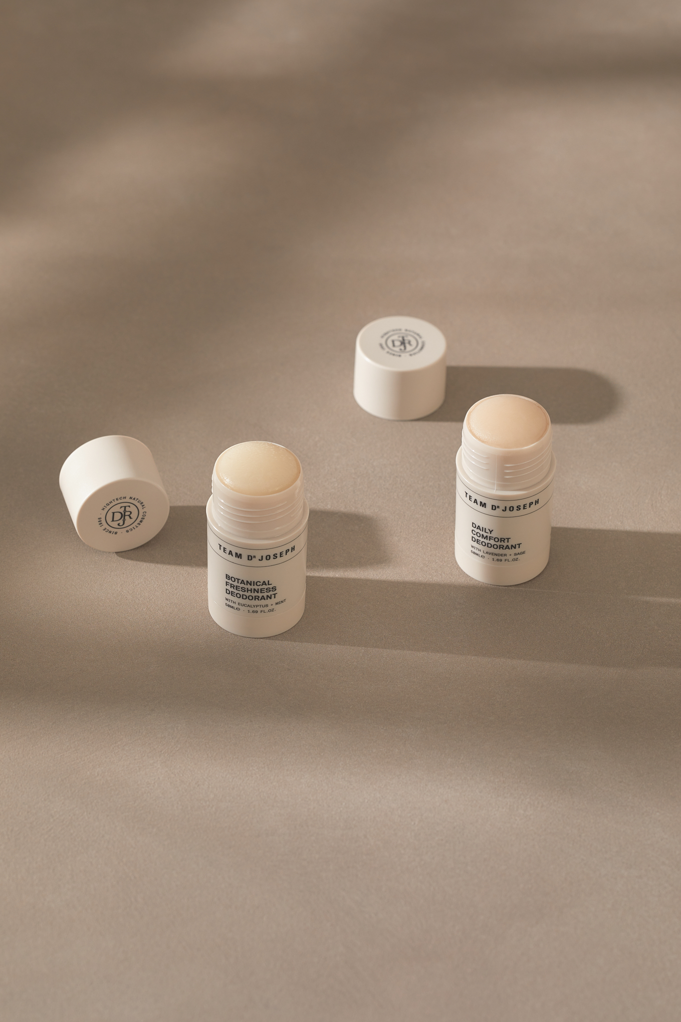 Four white tubes of Team D'Joseph deodorant, two with caps, are arranged on a neutral surface with soft shadows.