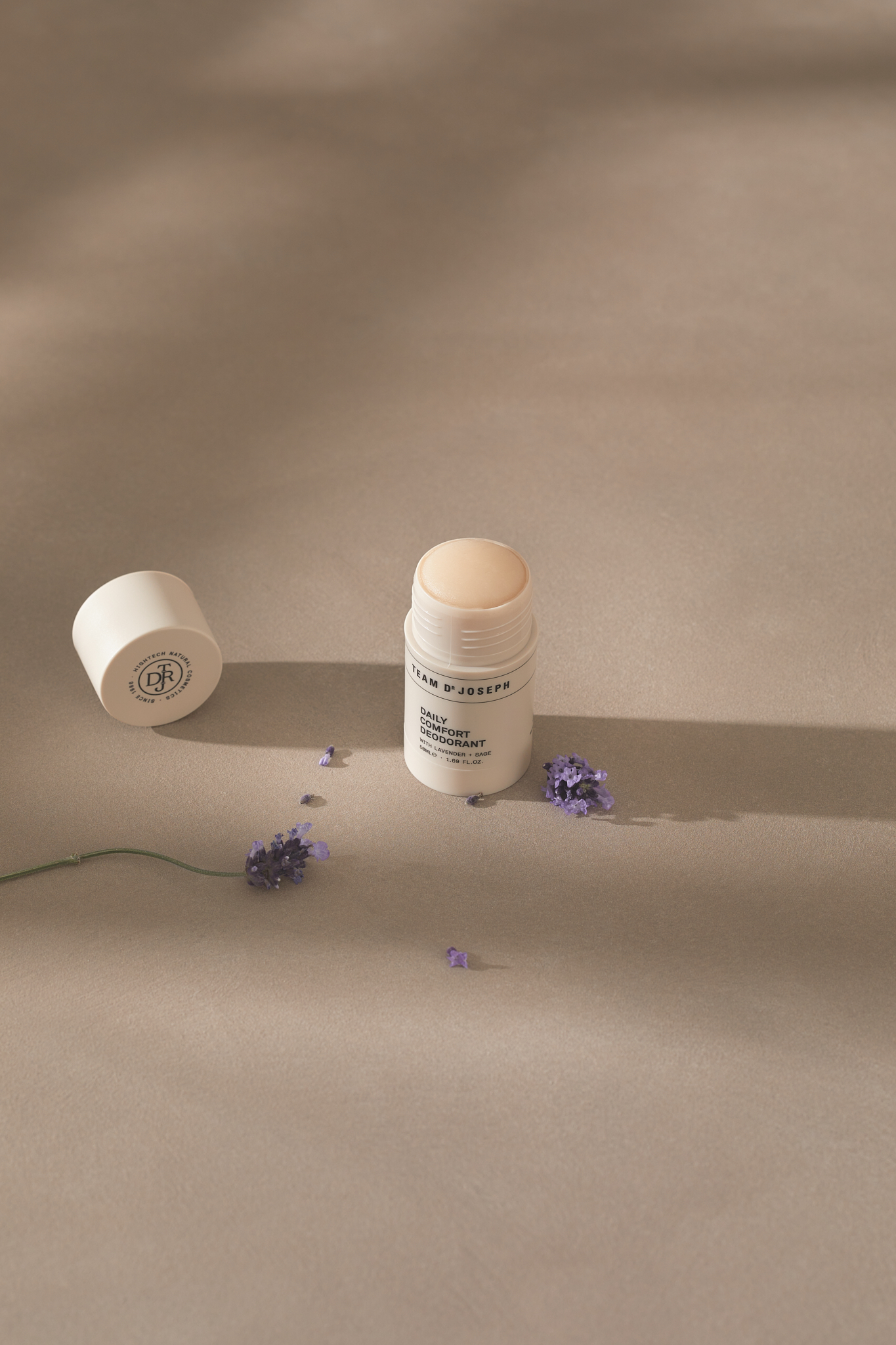 Still life shot of Balm P Joseph Daily Comfort Deodorant with purple flowers on a neutral surface, capturing beauty and skincare.