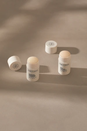 Two open white stick deodorants and matching screw caps arranged on a warm beige studio surface with soft shadows.