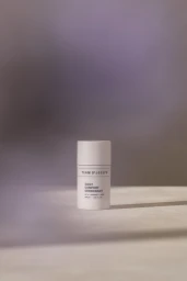 White Team Dr Joseph Daily Comfort Deodorant stick standing on a surface under soft directional light with a muted purple background.