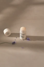 An open Team Dr Joseph stick deodorant with cap and purple lavender sprigs on a warm beige background.