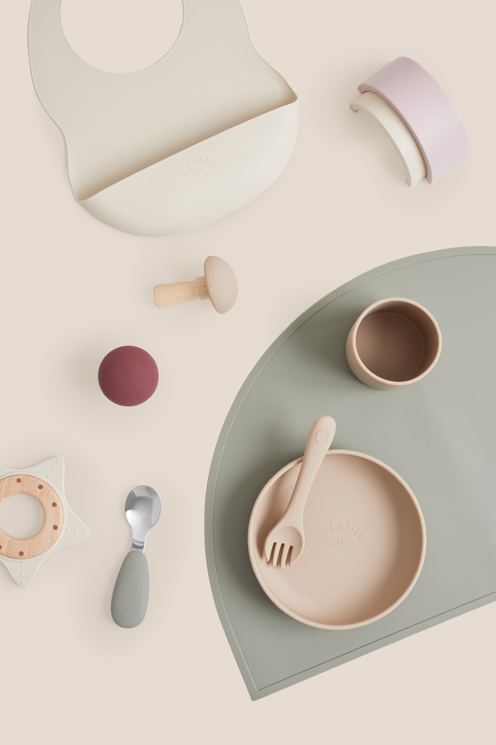 Still life of baby feeding and teething products in neutral tones on a beige background, arranged with a semi-circle mat.