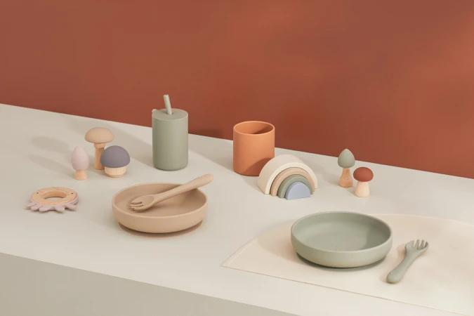 Neutral-toned tableware and toys including plates, cups, utensils, mushroom toys, and a wooden rainbow, set on a light surface.