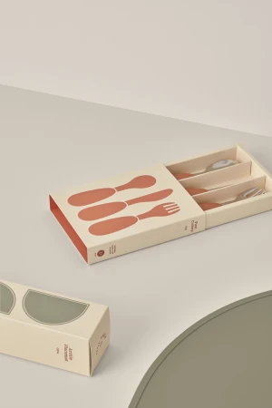 An eye-level studio shot presents a flatware set in a stylish box, accompanied by a matching placemat and another boxed item.