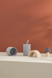 Silicone baby cups, a nesting rainbow, and a mushroom toy arranged on a ledge against a warm terracotta wall with soft shadows.