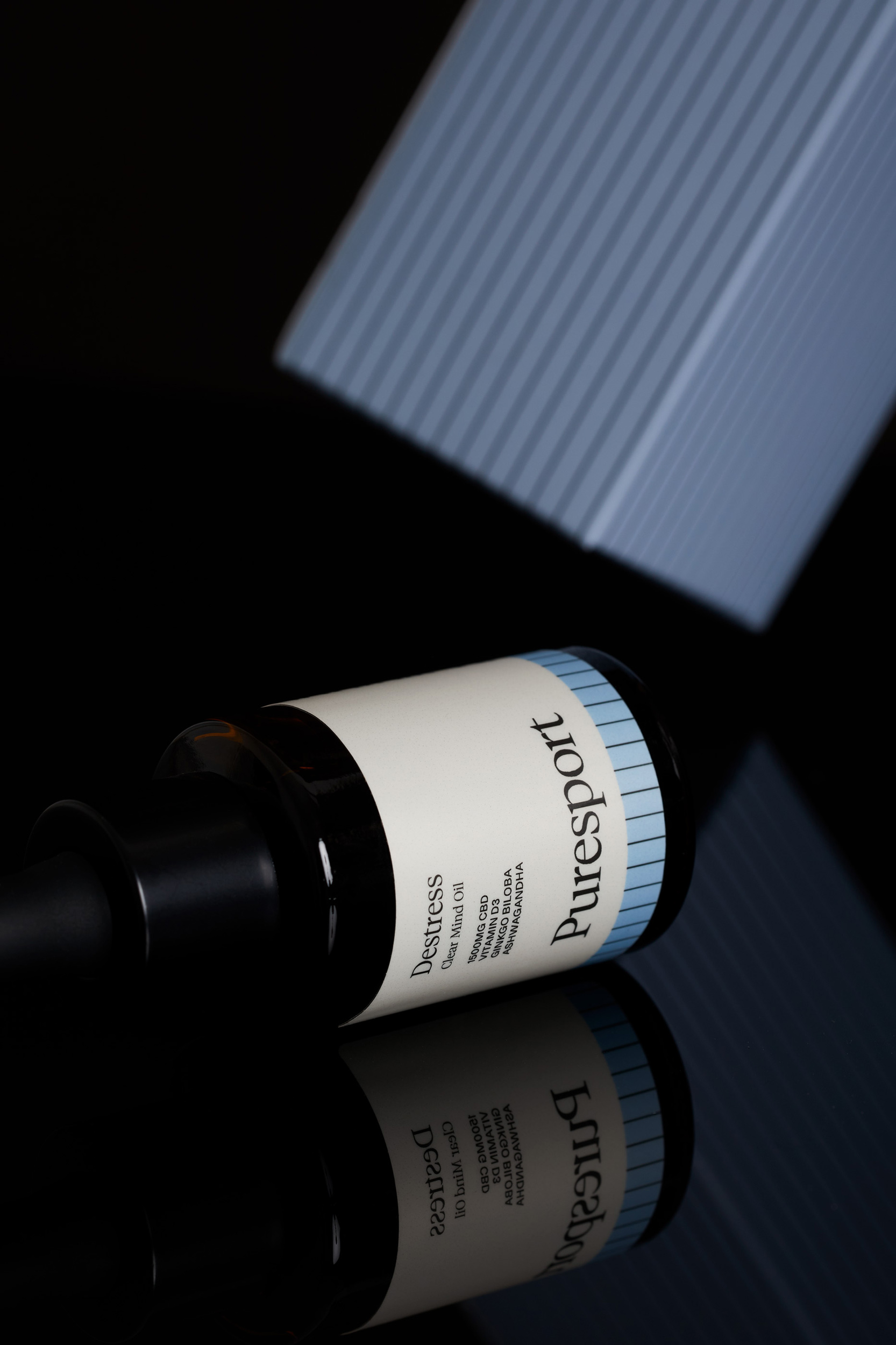Puresport Destress Time Release CBD oil bottle on a reflective black surface with packaging in soft, cool studio lighting.