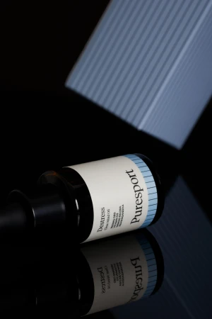 Puresport Destress Time Release CBD oil bottle on a reflective black surface with packaging in soft, cool studio lighting.