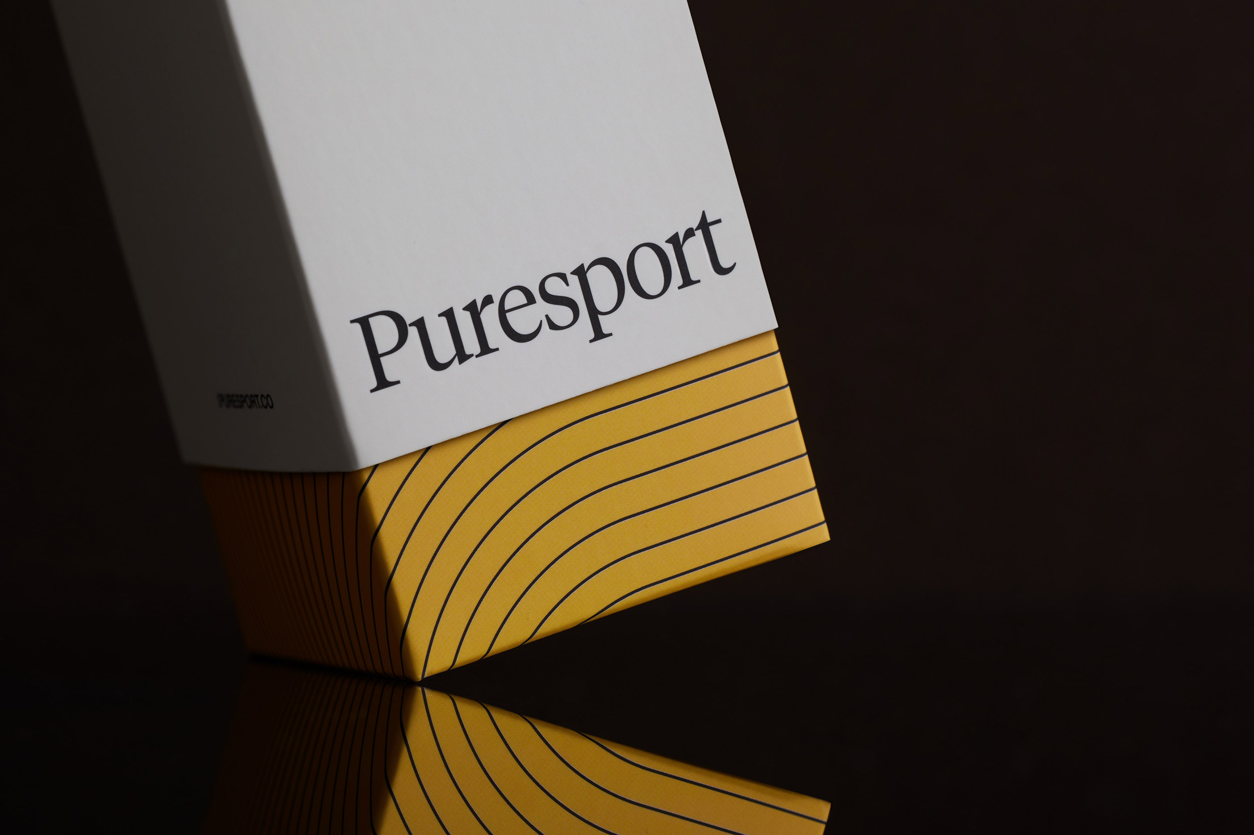 Product shot of a white and yellow Puresport box on a reflective dark surface, showcasing minimalistic design and packaging.