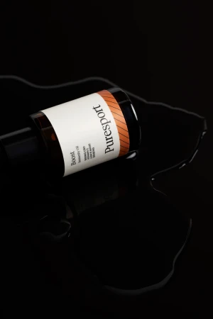 Elevated still life shot of a Puresport boost bottle on a wet black surface, showcasing the product's packaging and brand.