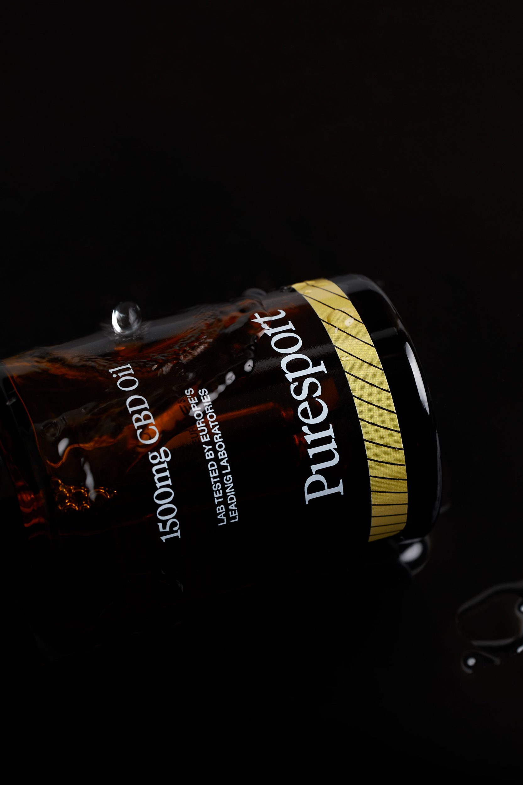 Close-up of a brown glass bottle of 1500mg CBD oil with water droplets against a black backdrop, highlighting the product label and details.